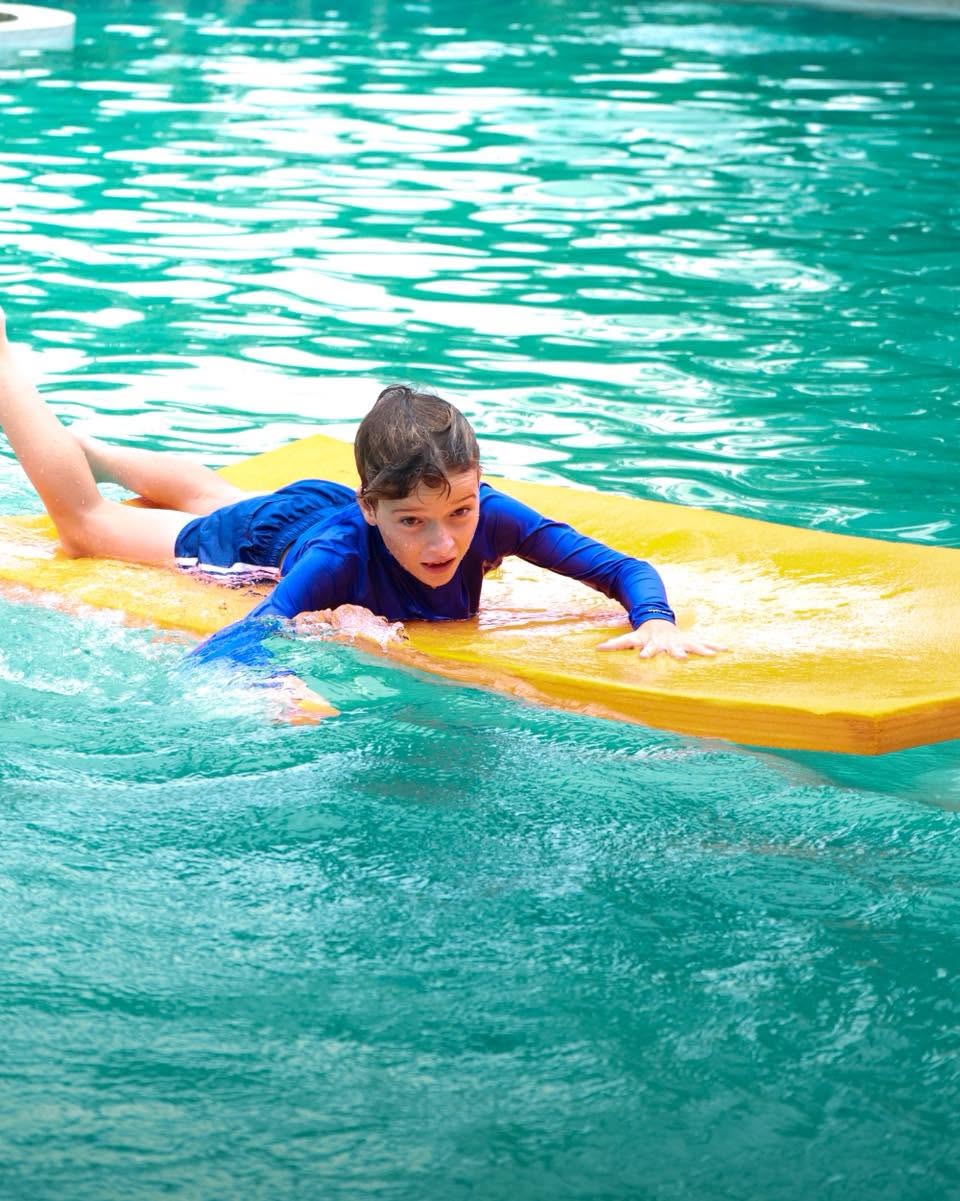 Lighthouse International School Student paddling with a board in the pool at YouTopia Phuket summer camp